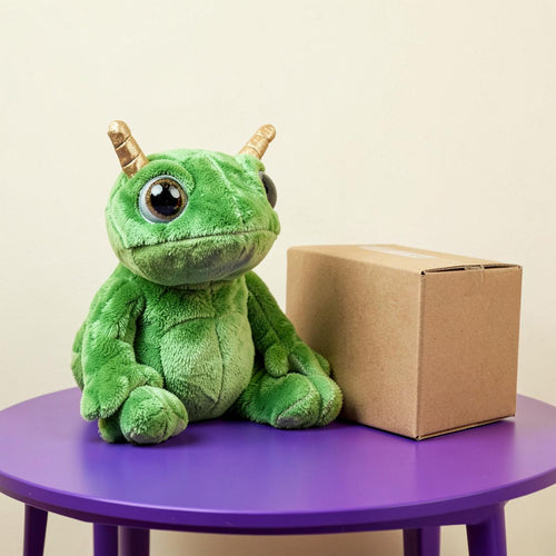 Cursed green alien frog plush toy next to a plain cardboard box